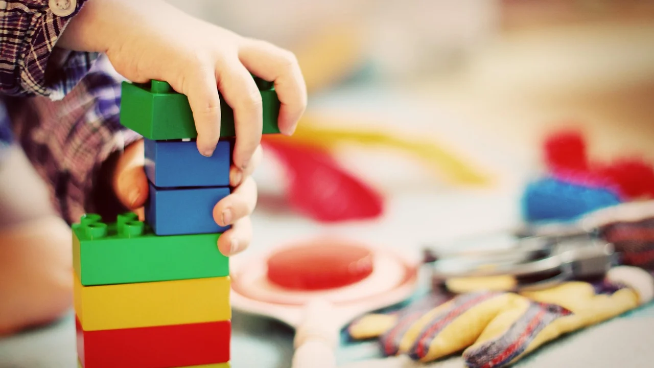Criança pequena empilhando blocos coloridos no chão
