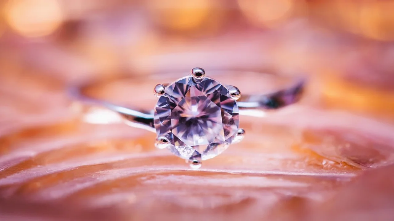 Anel com diamante em destaque sobre fundo neutro.